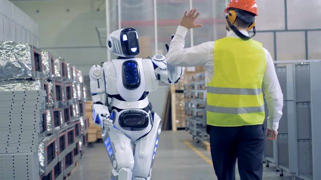 A robot goes towards a man and gives him a hi-five.