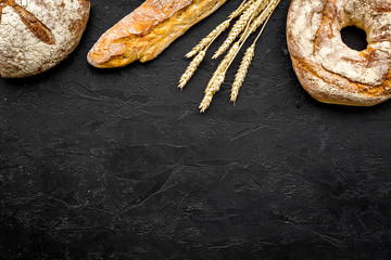 Appetizing fresh bread concept. Baguette and round loaf near ears of wheat on black background top view copy space