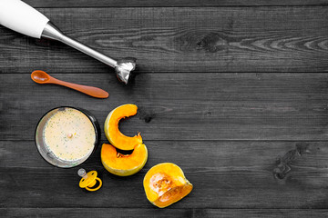 Make baby food at home. Puree with pumpkin near immersion blender and pacifier on dark wooden...