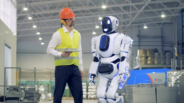 Male worker switches on a droid, then greets it in a factory facility. 4K.