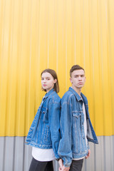 A beautiful couple dressed in denim jackets stands on the background of a yellow wall. Portert of a beautiful couple against the background of a colored wall