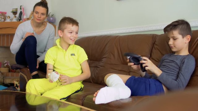 Two brothers with broken hand and leg are fooling at home sitting on sofa