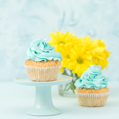 Cupcake with blue cream decoration on vintage stand and bouquet of yellow chrysanthemum in glasses vase.