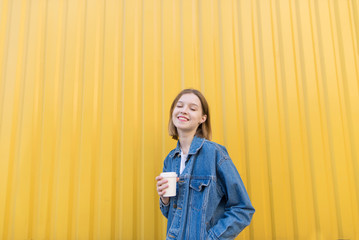 Happy girl with a cup of coffee on a yellow background. Portrait of a girl with her eyes closed and with a cup of coffee in her hands behind the background of the yellow wall.