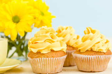 Cupcake with yellow cream decoration, coffee with milk and bouquet of yellow chrysanthemum in small glass cup.