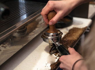 Barista making fresh takeaway coffee. Close-up view on hands with portafilter, barista coffee preparation service concept.	