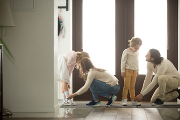 Parents helping children son and daughter put shoes on or take off in hall getting ready to go out...