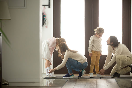 Parents helping children son and daughter put shoes on or take off in hall getting ready to go out together or coming back home from walk, care and good relations in happy family with kids concept