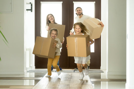 Excited kids holding boxes running entering into new big house, cute children boy and girl carrying belongings helping parents exploring own home, happy family on moving day and relocation concept