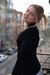 Obraz premium Portrait of a young woman in a black suit close-up against a background of a blurry city in the rays of the setting sun.