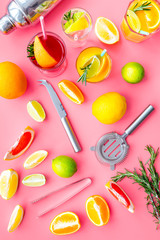 Bartender workplace for make fruit cocktail with alcohol. Shaker, strainer and other bar tools near citrus fruits and glass with cocktail on pink background top view pattern