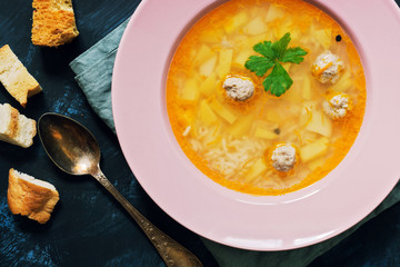 Turkish soup with meatballs close-up. Dietary soup is served in a pink plate on a blue background. View from above.