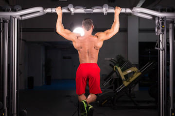 Fototapeta na wymiar Athlete muscular fitness male model pulling up on horizontal bar in a gym.