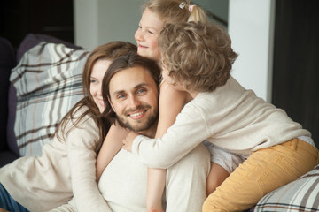 Smiling man looking at camera enjoying kids and wife embracing dad, happy loving family parents and children having fun bonding together on sofa hugging congratulating daddy with fathers day at home