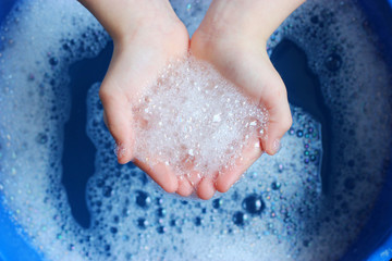 soap foam in the hands of the child on a beautiful blue background. Hand hygiene. Children's hygiene. 