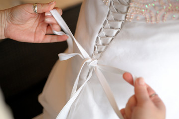Obraz na płótnie Canvas Women's hands tie a ribbon on the corset of a wedding dress. Morning gathering of the bride.