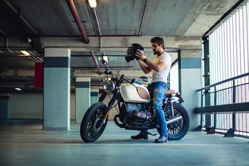 Printed kitchen splashbacks Motorcycle Man putting on motorcycle helmet in a garage