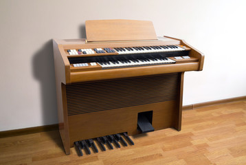 Old-fashioned double-keyboard electric organ standing by a wall in a room