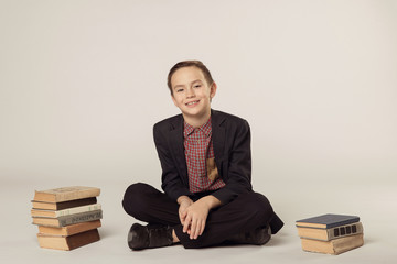 Cute boy in a suit sitting on a white background. pile of books.