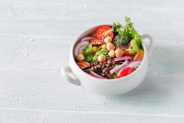 Vedan Chickpeas Salad with black quinoa, chia seeds, broccoli, tomatoes, spinach and nuts in white dishes on old light blue concrete background. Clean eating, superfood, detox food concept