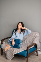 Obraz premium Portrait of beautiful sexy and attractive young pretty brunette woman posing in blue jeans and shirt on the blue sofa. Sofa relax concept after hard working day