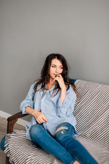Portrait of beautiful sexy and attractive young pretty brunette woman posing in blue jeans and shirt on the blue sofa. Sofa relax concept after hard working day