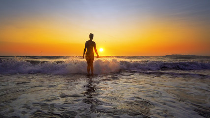 Fototapeta na wymiar Cinematic shot of sexy woman walking on water at sunset on ocean beach, steadicam shot