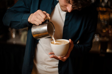 Young barista pouring some milk into a coffee cup