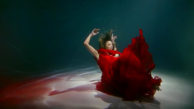 young girl in long red dress plunges to the bottom underwater