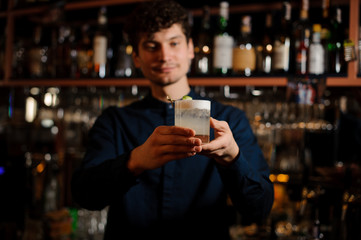 Young curly barman holding a glass with fresh and sour summer cocktail