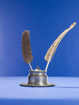 Quill pens and inkwell on blue background