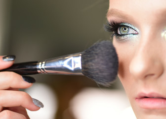 Beautiful young girl with blue eyes posing with tassel for applying makeup. Closeup portrait of model