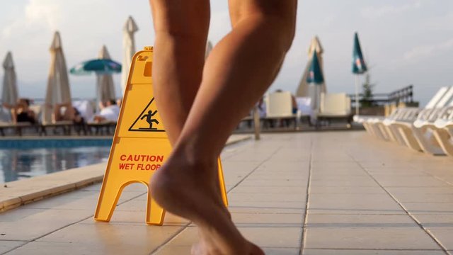 Muscular man walk on pool tiled side with Caution wet floor sign