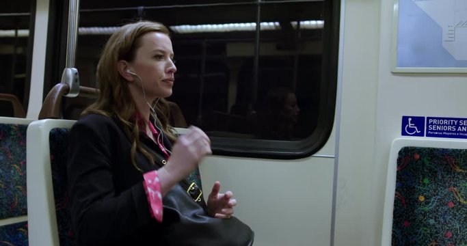 MS smartly dressed business woman sitting on subway train, listening to music on headphones. Hand-held, slow motion 4K 60fps. No logos or branding visible