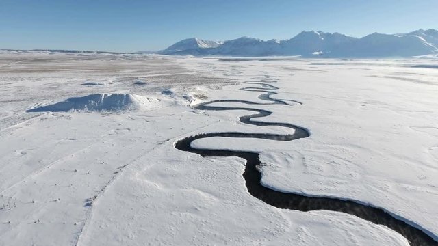 Aerial shot of a winding river running through a snow covered landscape