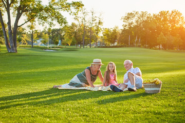 Girl with grandparents having picnic. People relaxing in summer park.