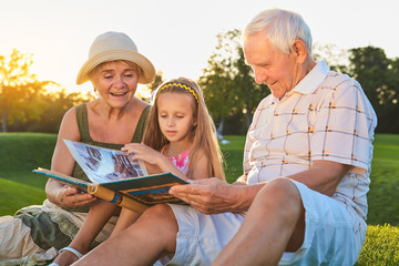 People looking through photo album. Caucasian girl with grandparents outdoors. Pages of the past.