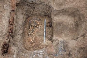 Archaeological excavations. Top view of the burial of a person, bones, skull with two ritual ceramic pots and a scale ruler.