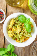 Pasta with chicken pieces and pesto sauce on an old wooden table.