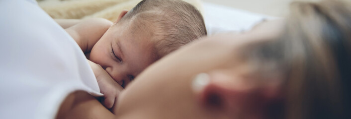 Newborn baby girl lying on the bed embraced by her mother. Selective focus on baby in background