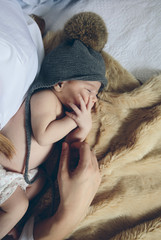 Newborn baby girl sleeping lying on a blanket on the bed next to her mother's hand