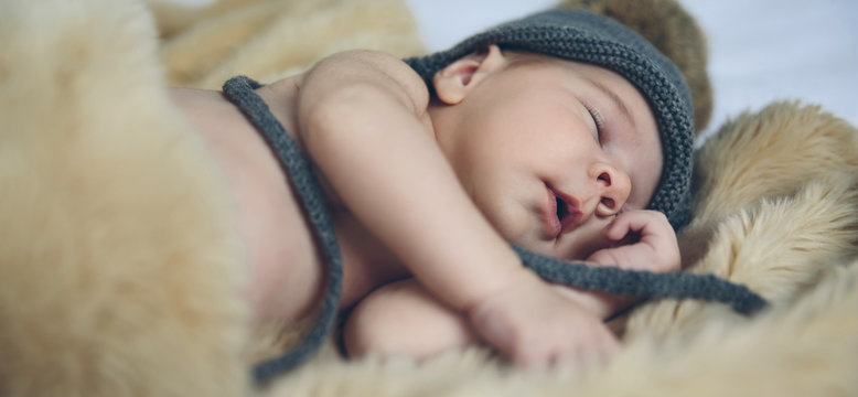 Newborn baby girl with pompom hat sleeping on a blanket