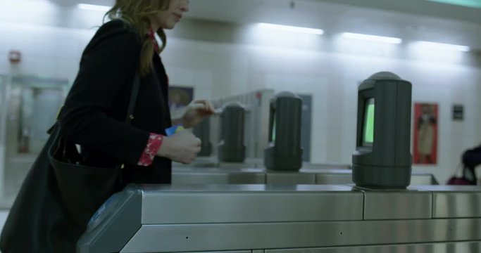 Detail shot, business woman's hand taps subway pass as she walks through turnstile entrance to trains. Hand-held, slow motion 4K 60fps.