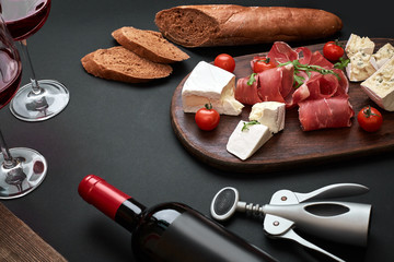 Obraz na płótnie Canvas Wine bottle with cheese and traditional sausages on wooden board on black background with copy space
