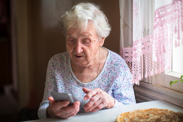 Elderly woman sits with a smartphone in her hands..