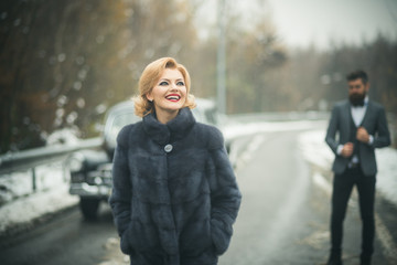 Retro woman in coat on road. Couple in love on romantic date. Bearded man and sexy woman in fur coat. Escort of girl by security. Travel and business trip or hitch hiking.