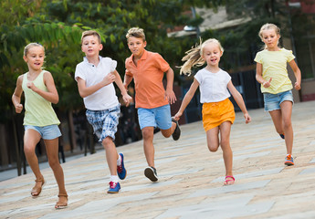 Fototapeta premium Group of cheerful children running together in town on summer