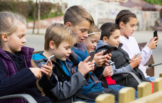 Kids sitting on bench with smartphones