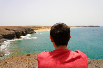 Back view of a sitting man enjoying Lanzarote landscape at Playas de Papagayo, Canary Islands