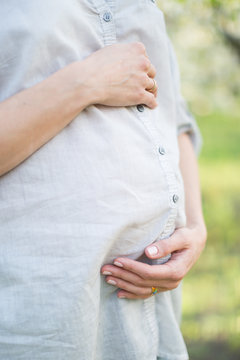 birth giving, anniversary, womanhood concept. close up of belly of pregnant woman who is wearing minimalistic cotton shirt in blue colour, she is hugging her tummy